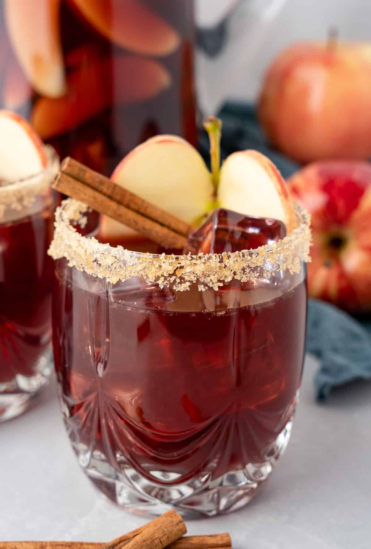 Apple Cider Sangria in glass rimmed with brown sugar and garnished with apple and cinnamon stick.