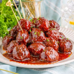 Square image of finished meatballs on plate with parsley and toothpicks