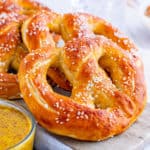 Square image of pretzels on marble board with mustard dip next to it