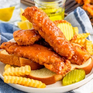 Square image of Chicken Tenders stacked on bread with pickles and french fries.