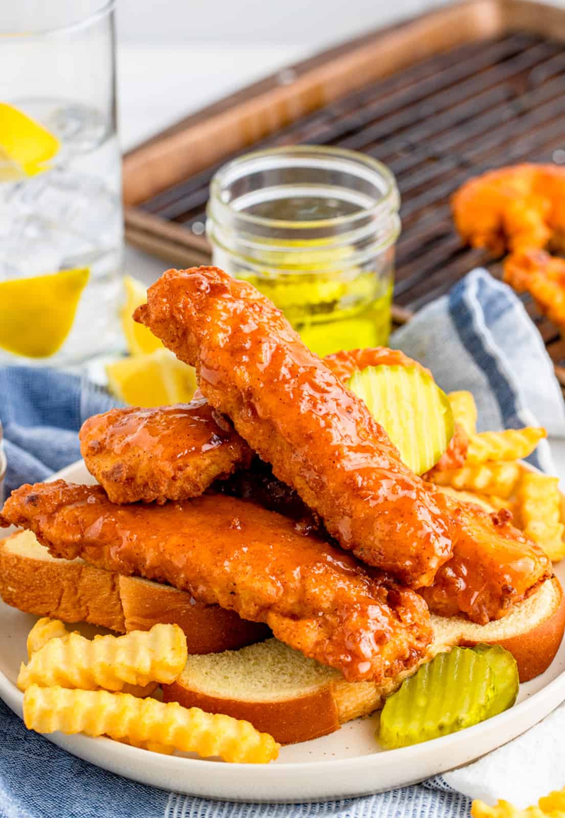 Nashville Hot Chicken Tenders stacked on plate with bread, fries and pickles.
