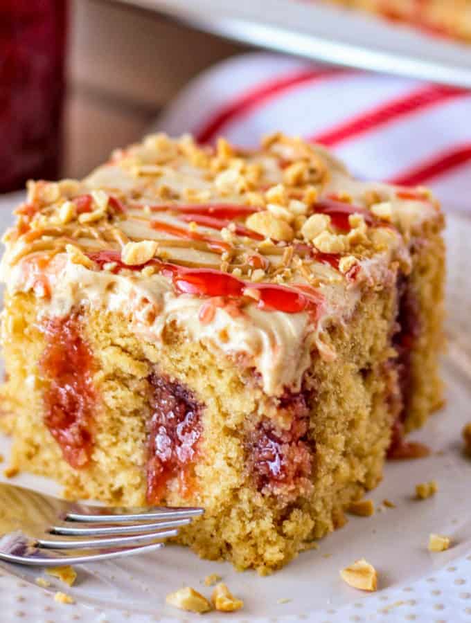 Square image of Peanut Butter and Jelly Poke Cake slice on white plate with fork.