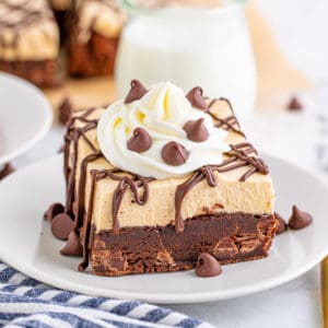 Square image of Peanut Butter Brownie on white plate with whipped topping and chocolate chips.