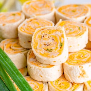 Close up square image of finished pinwheels stacked on top of one another with green onions on the side.