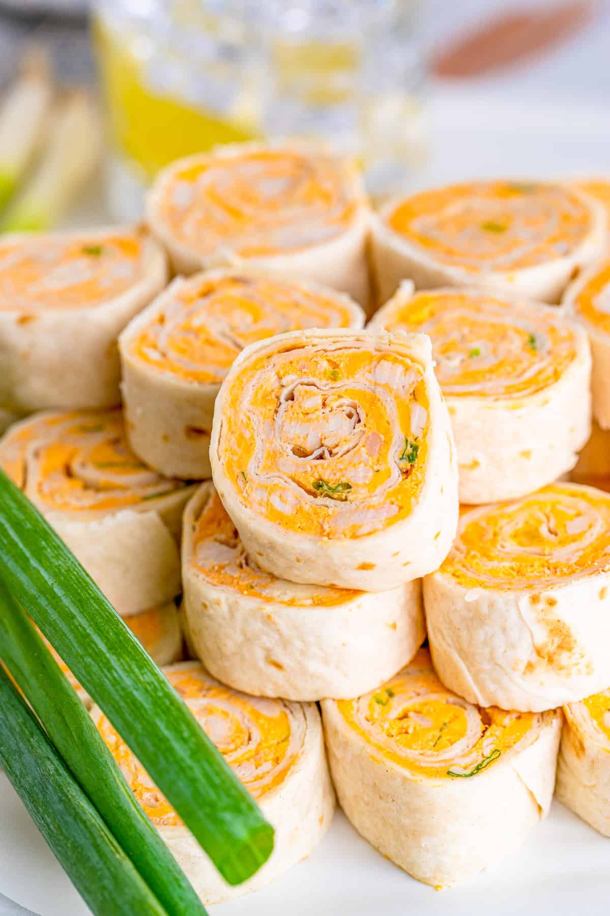 Finished Buffalo Chicken Pinwheels stacked on top of one another on white tray with green onions to the side.