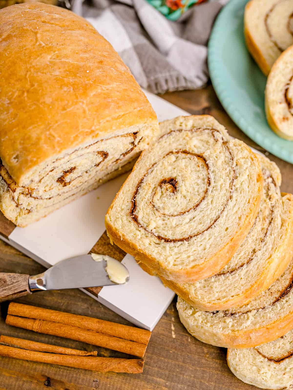 Overhead of slices of Cinnamon Swirl Bread stacked over one another with butter knife and cinnamon sticks.