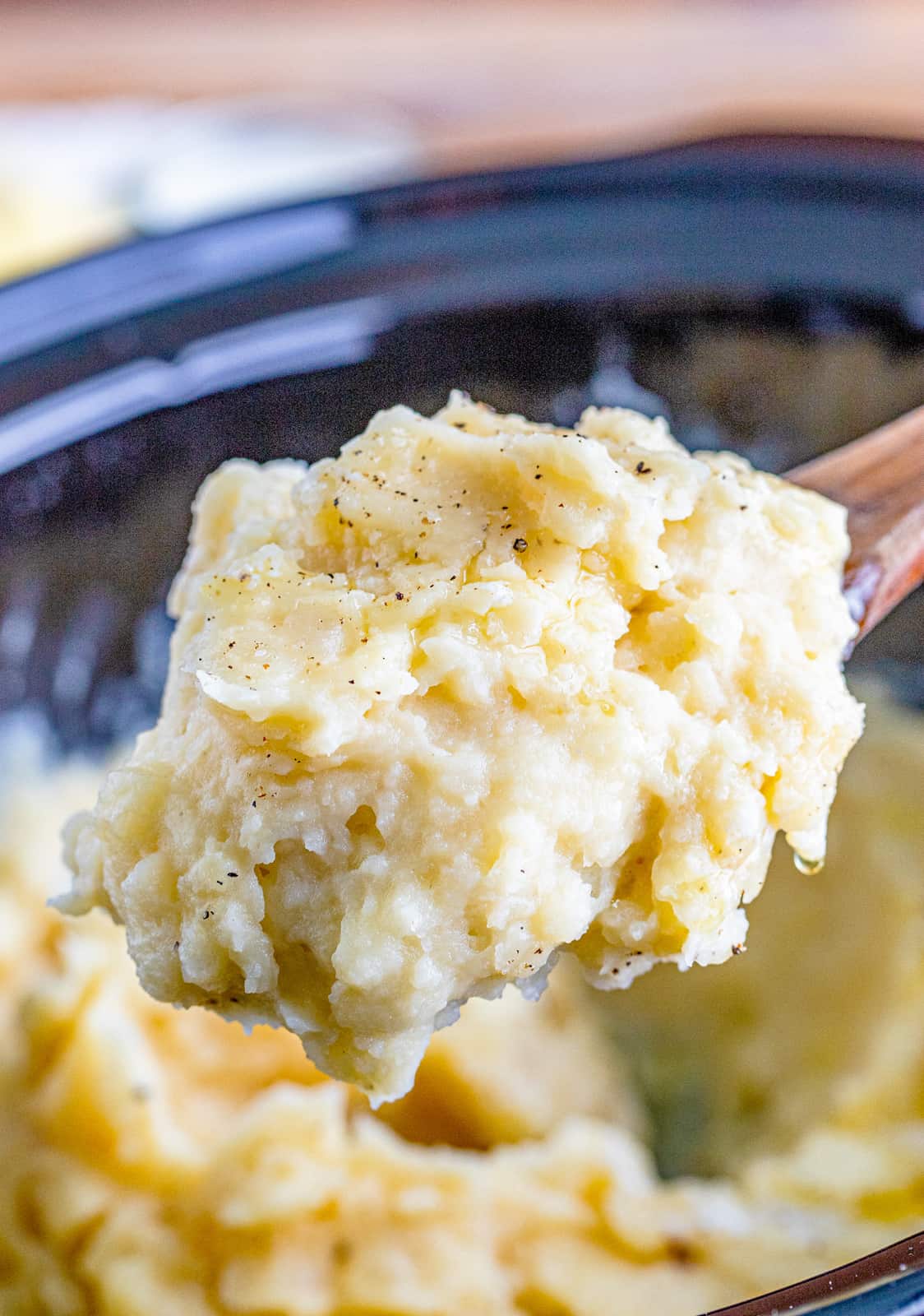 Wooden spoon lifting up some of the Crockpot Mashed Potatoes out of crockpot.