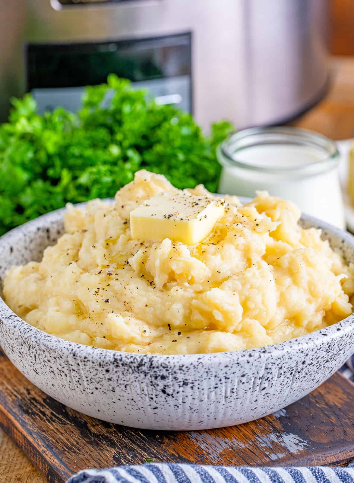 Crockpot Mashed Potatoes in serving bowl with parsley and crockpot in background.