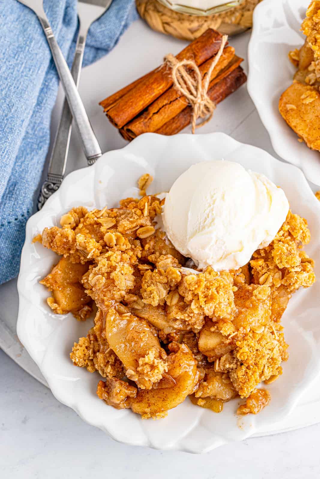 Overhead photo of Easy Apple Crisp on white plate with ice cream and cinnamon sticks next to plate.