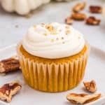 Close up square image of cupcake on white plate with chopped nuts.