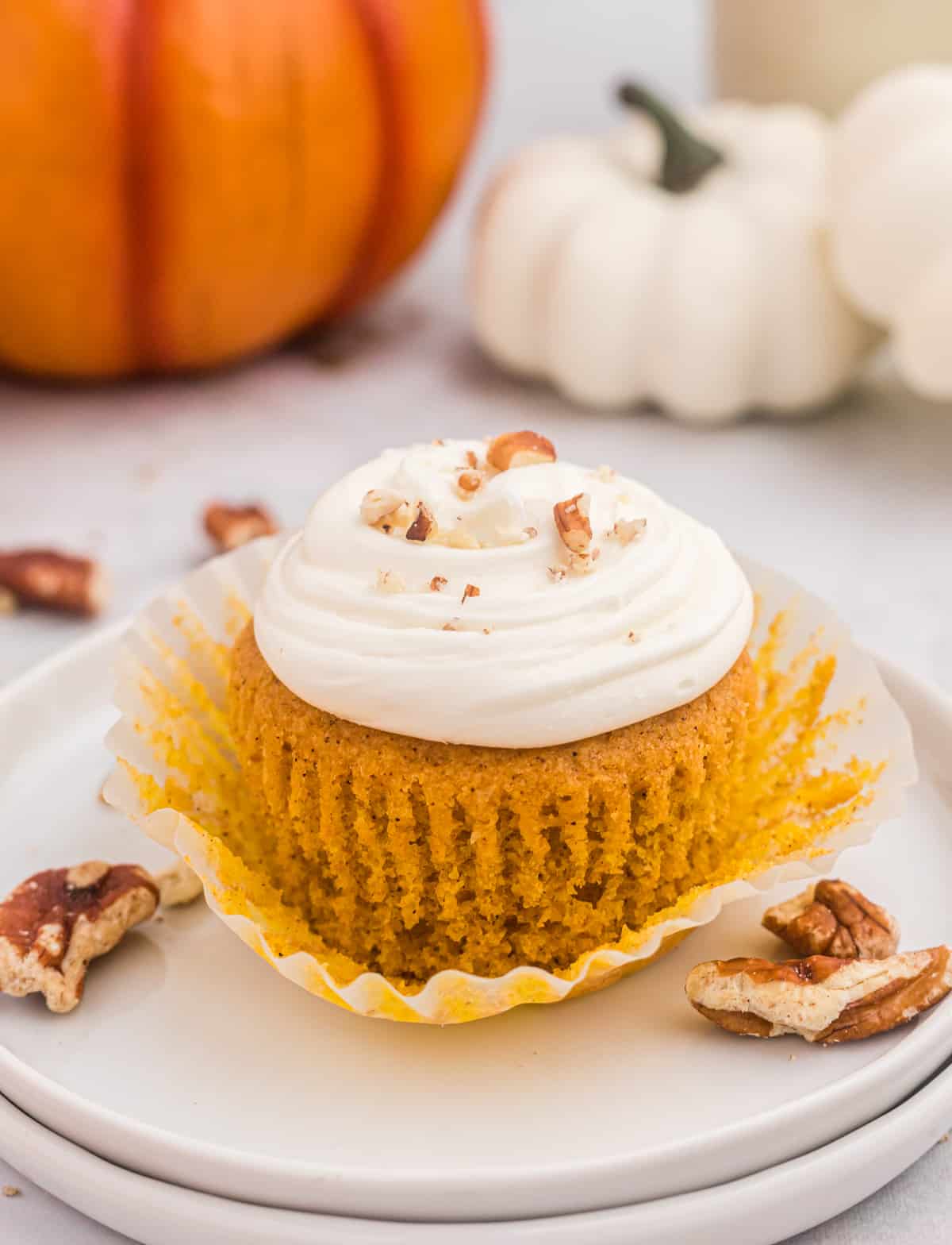 One of the Pumpkin Cupcakes on white plate with the cupcake liner pulled down showing the full cupcake.