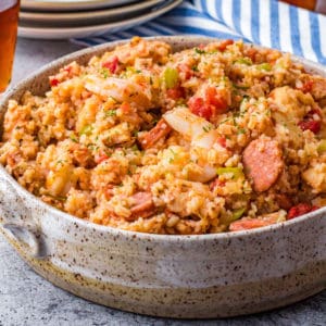 Square serving bowl of Jambalaya with plates in background.