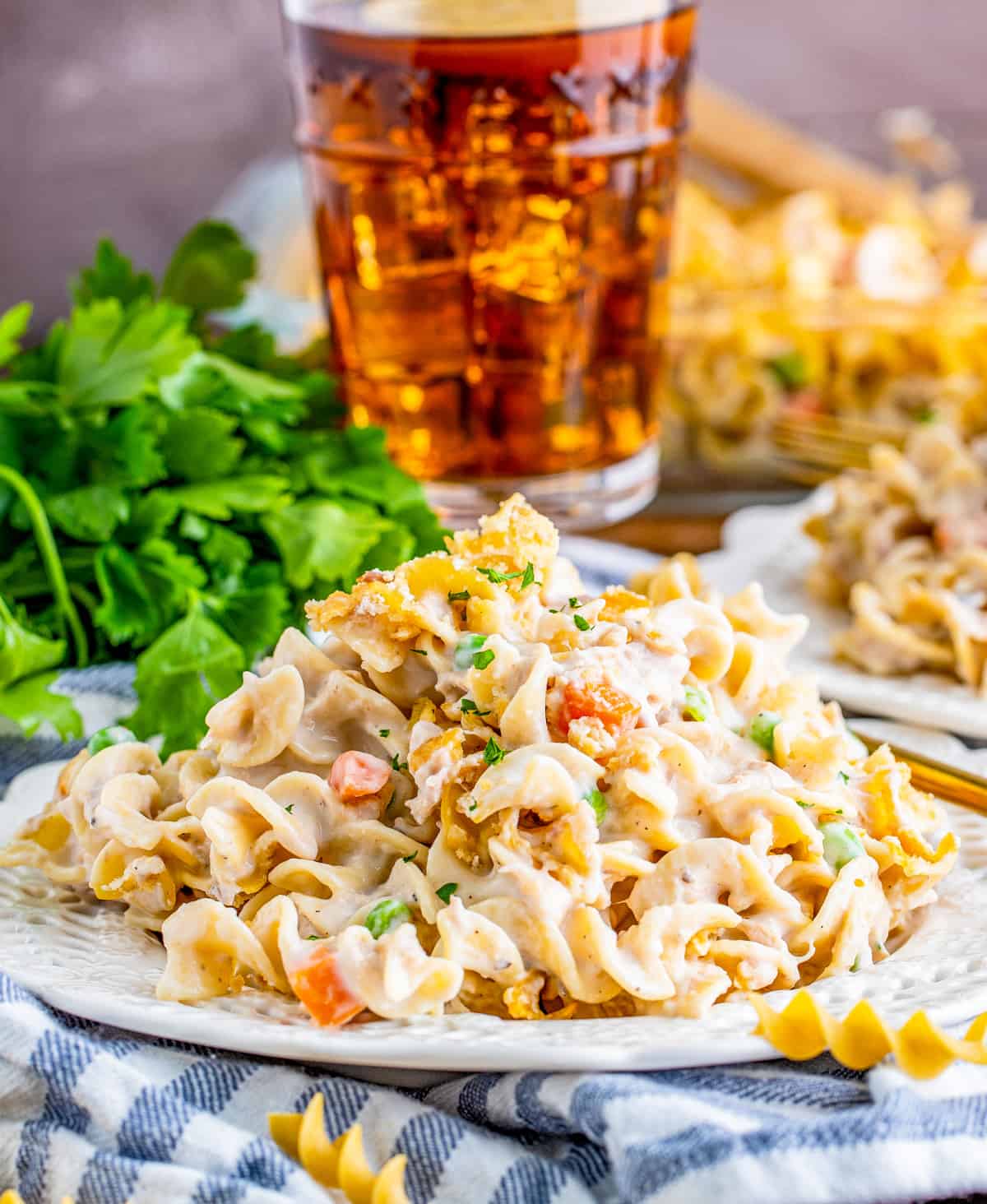 Tuna Noodle Casserole Recipe on white plate with parsley and a drink in the background.