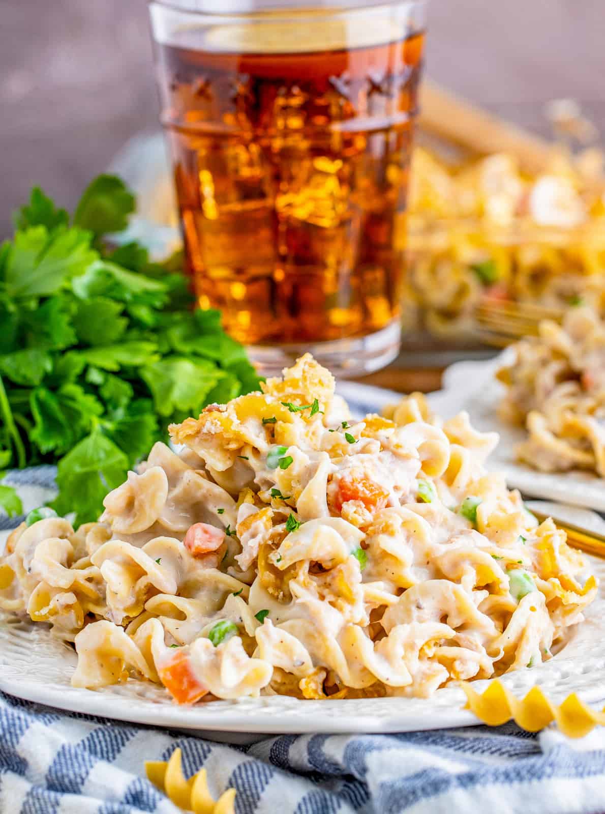 Tuna Noodle Casserole Recipe on white plate with parsley and drink in background.