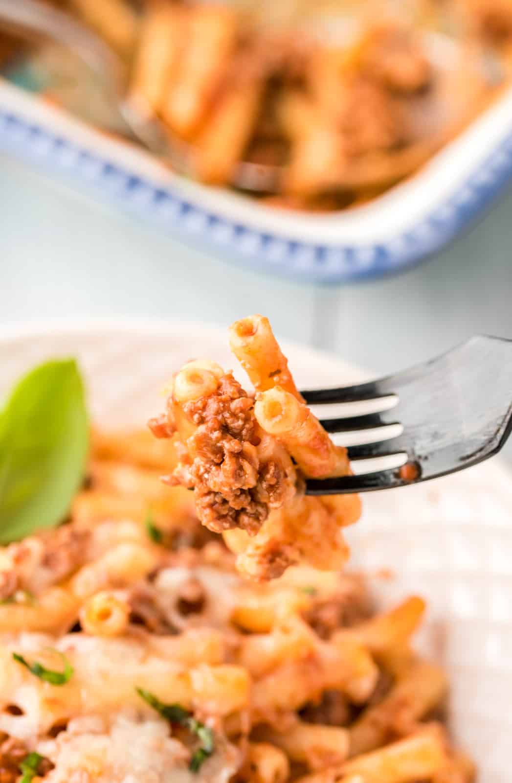 Fork holding up a bite of Baked Ziti Recipe out of bowl.