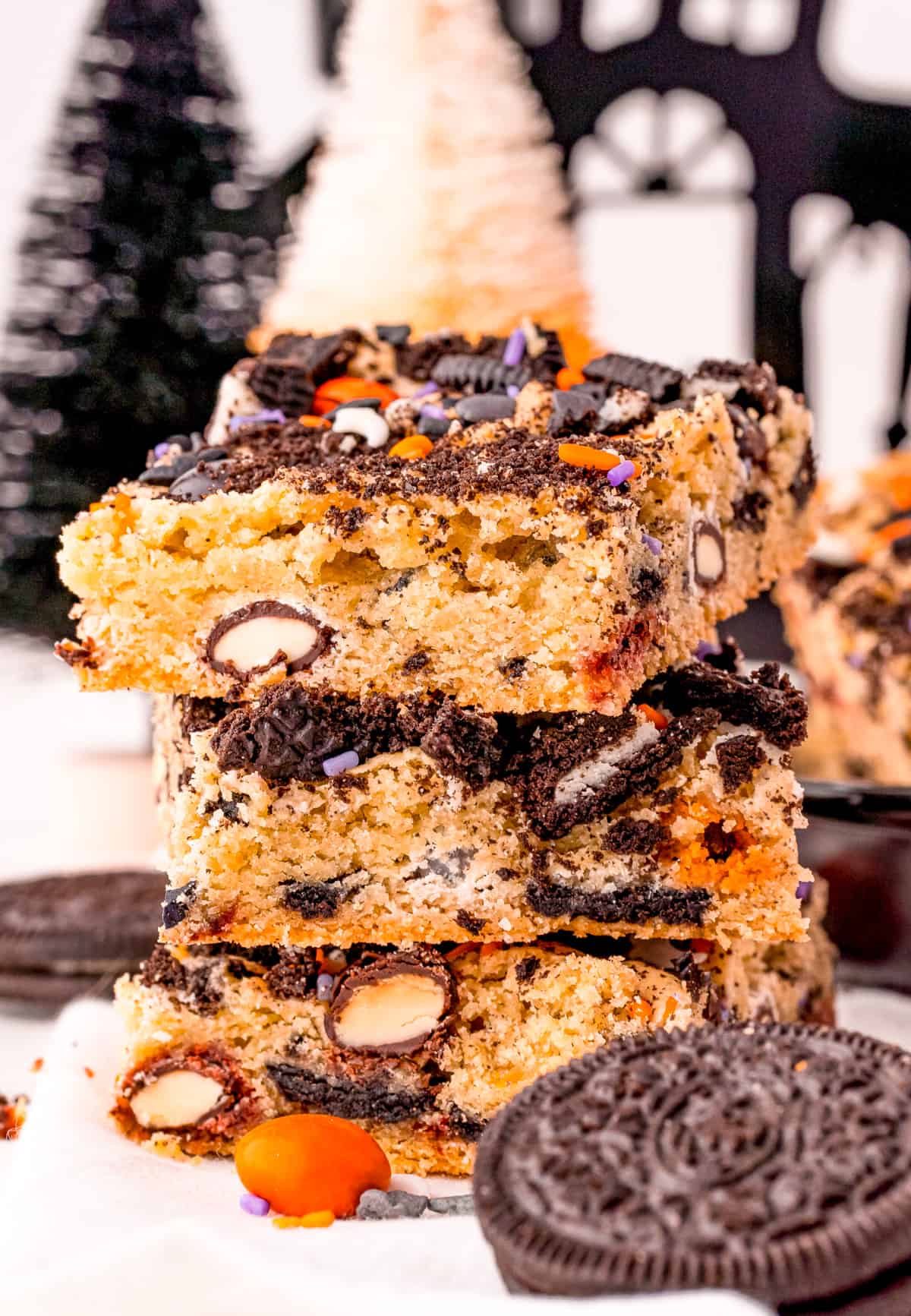 Stacked Halloween Cookie Bars on white surface with Halloween decor in background.