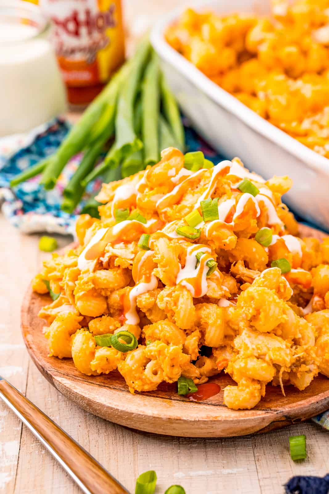 Buffalo Chicken Mac and Cheese on wooden plate garnished with buffalo sauce, ranch and green onions.