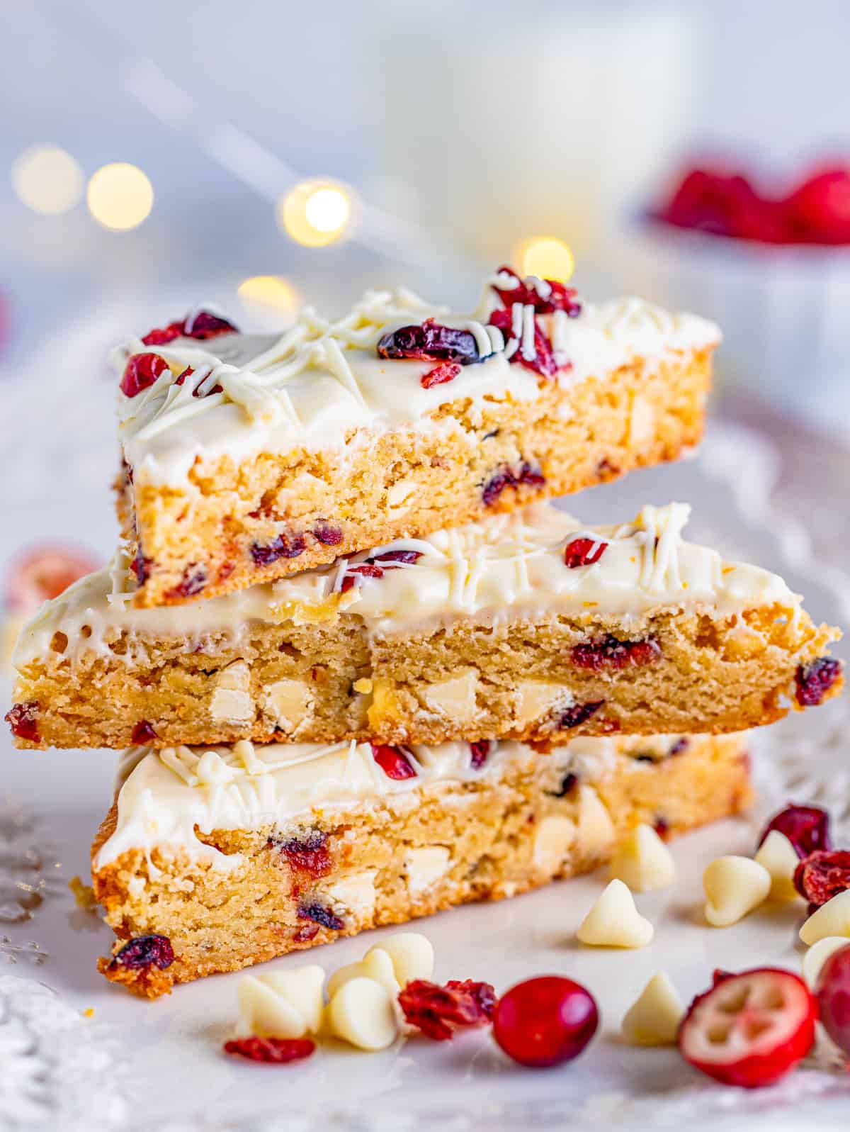 Three stacked Cranberry Bliss Bars with white chocolate chips and cranberries beside them.