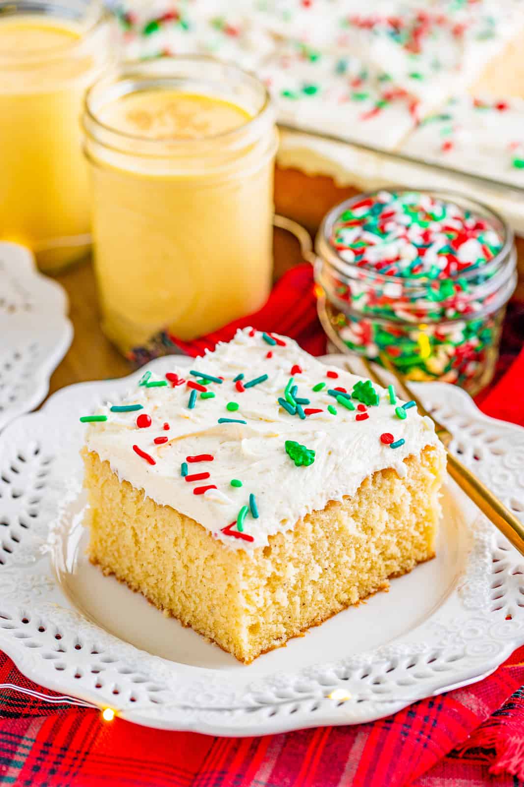 Eggnog Cake slice on white plate with sprinkles and eggnog in background.