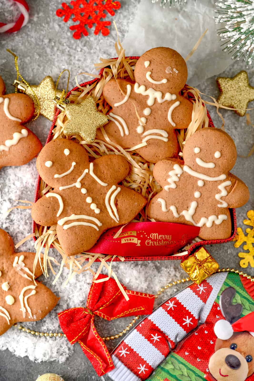Three Gingerbread Men Cookies in small box with holiday decorations.