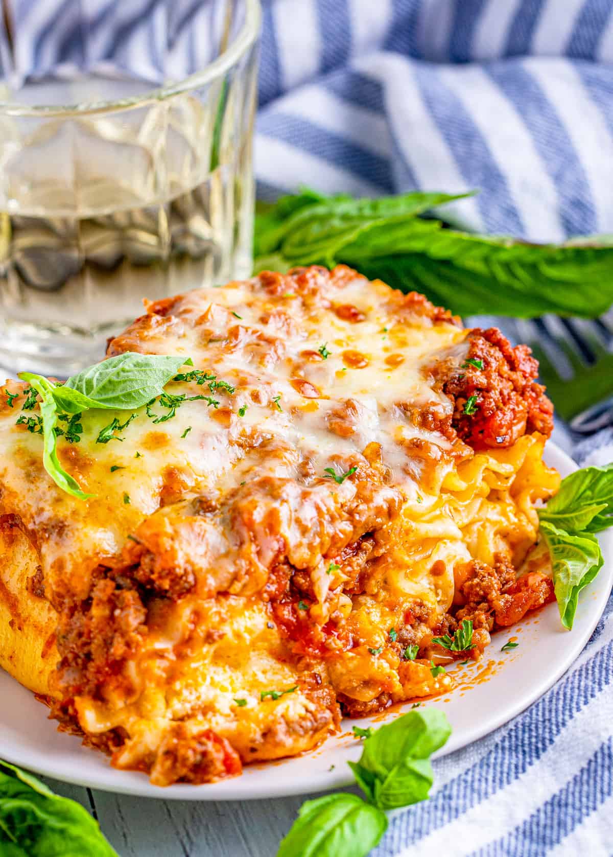 Lasagna Rolls on white plate with basil leaves and glass of water in background.