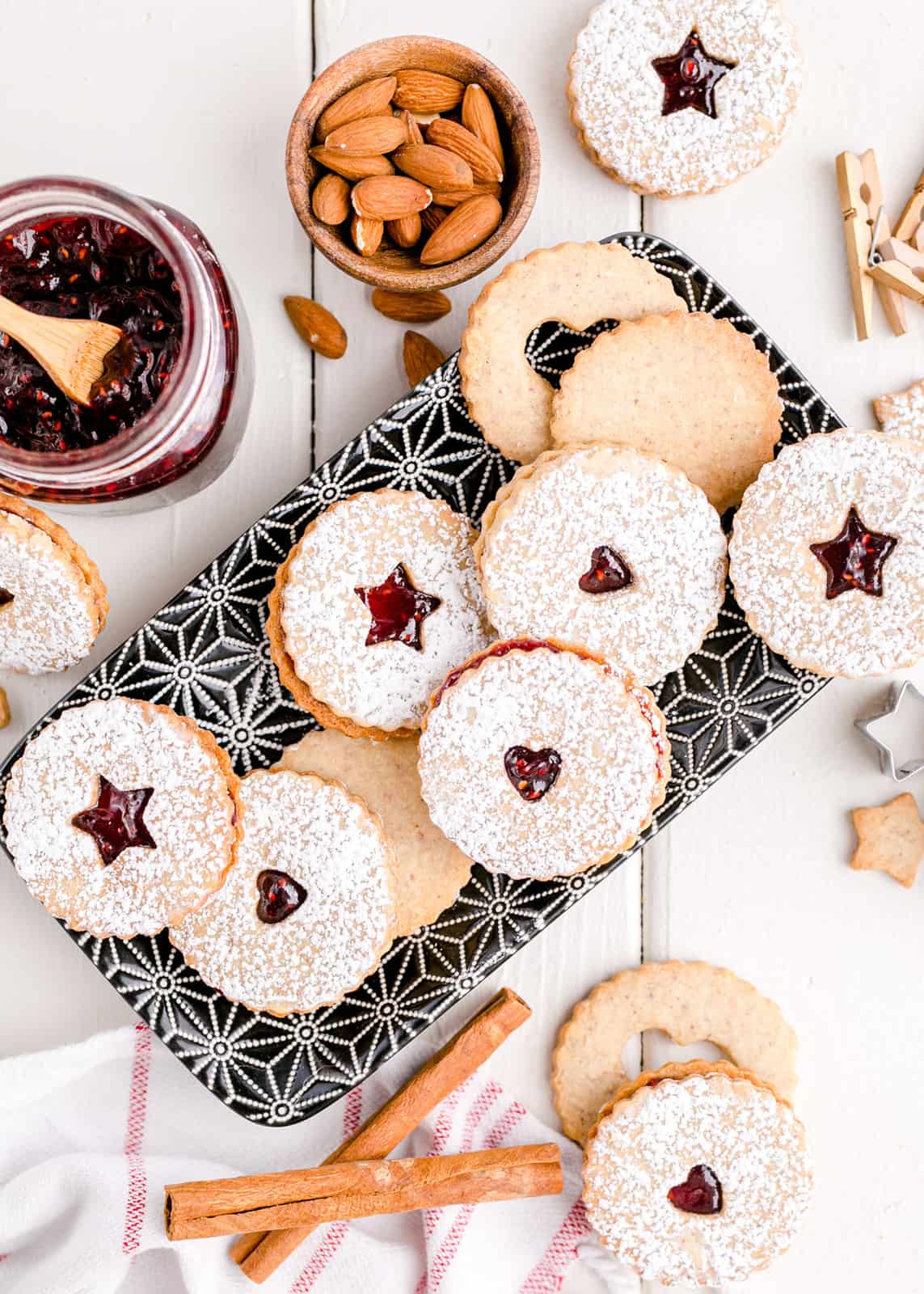 Overhead of Linzer Cookies on tray with almonds, jam and cinnamon sticks.
