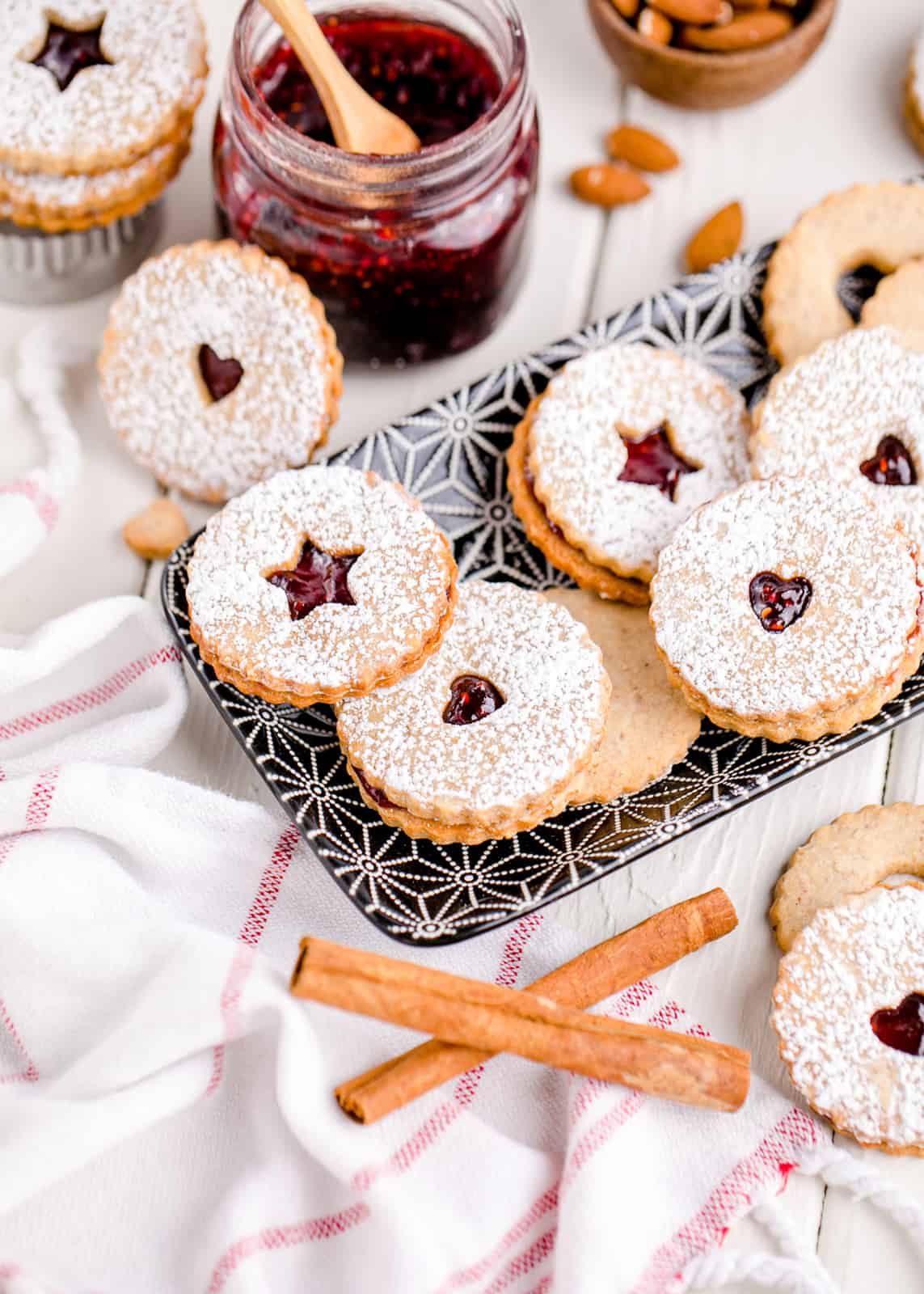 Linzer Cookies on tray stacked next to jam with cinnamon sticks.