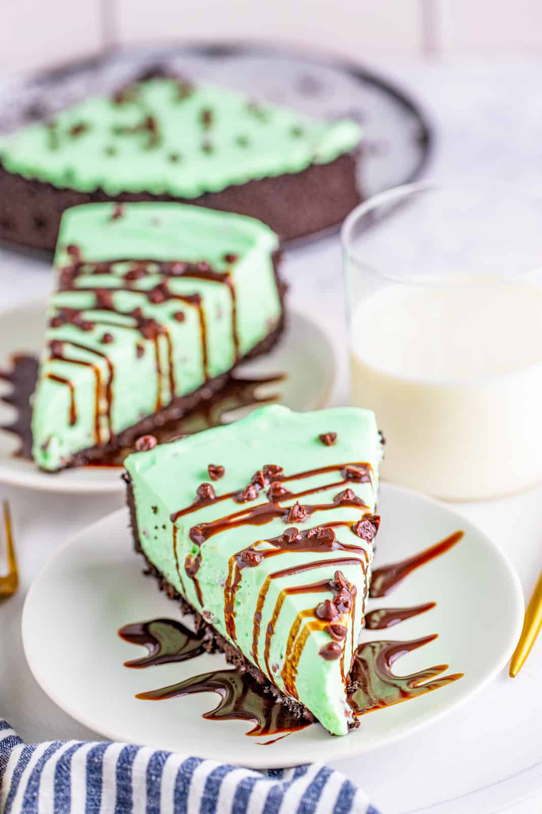 Two slices of No Bake Mint Chocolate Cheesecake on white plates with glass of milk.