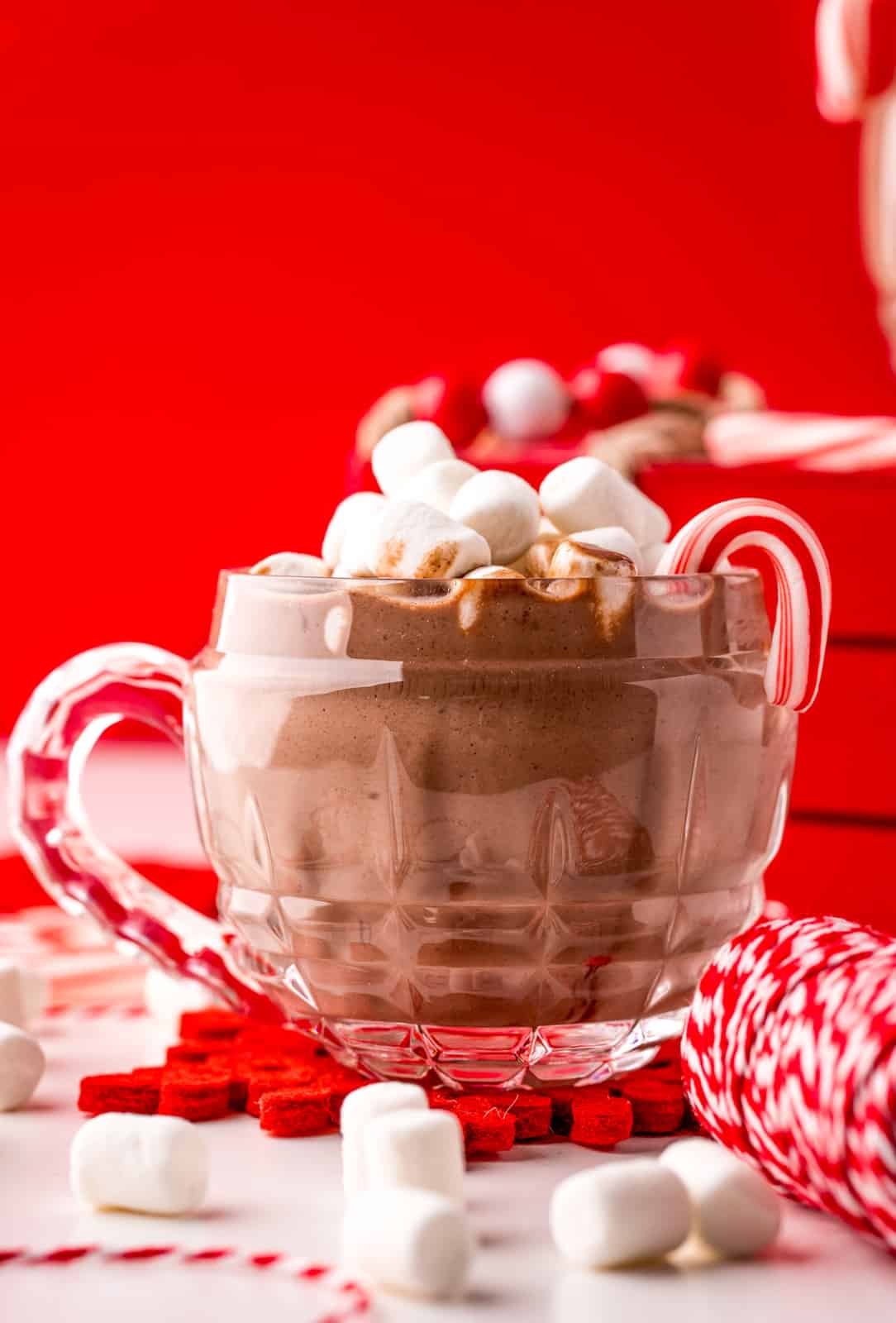Straight on photo of Hot Chocolate in clear mug with candy cane and marshmallows.
