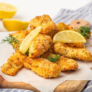 Square image of fish sticks stacked with lemon wedges and dill.