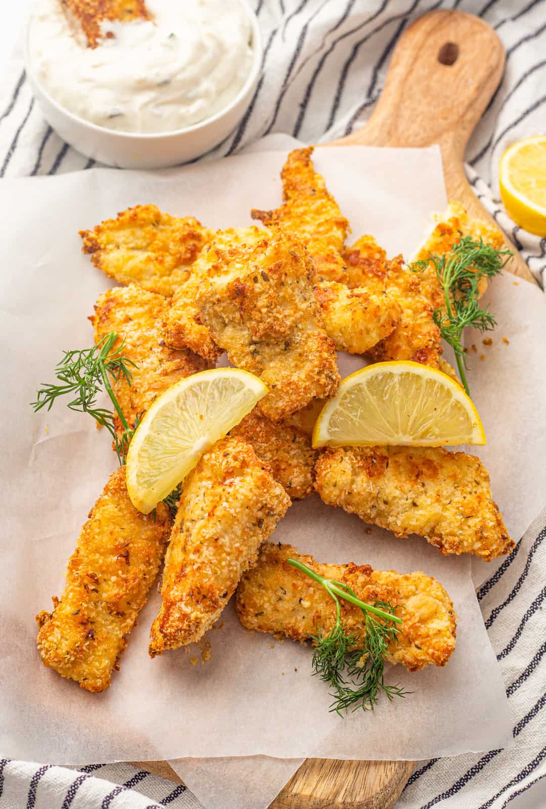 Overhead of Air Fryer Fish Sticks on parchment paper covered cutting board with lemon and dill.