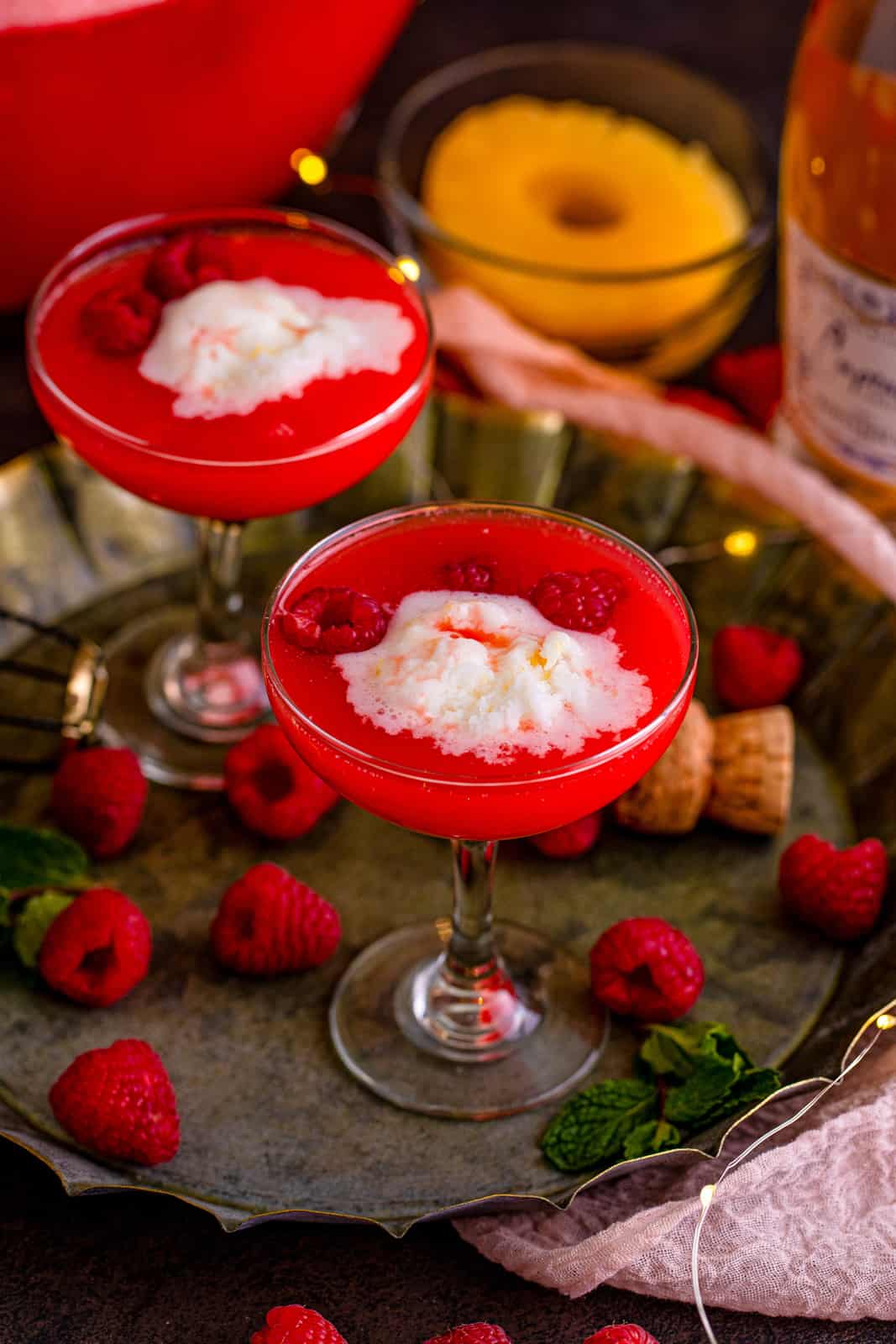 Two glasses of Boozy Pineapple Punch no tray with raspberries.
