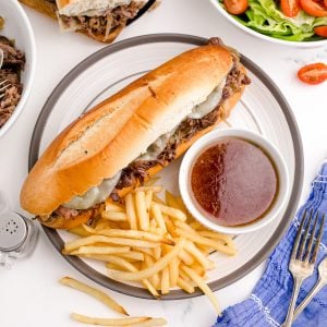Square photo of sandwich on plate with french fries and au jus.