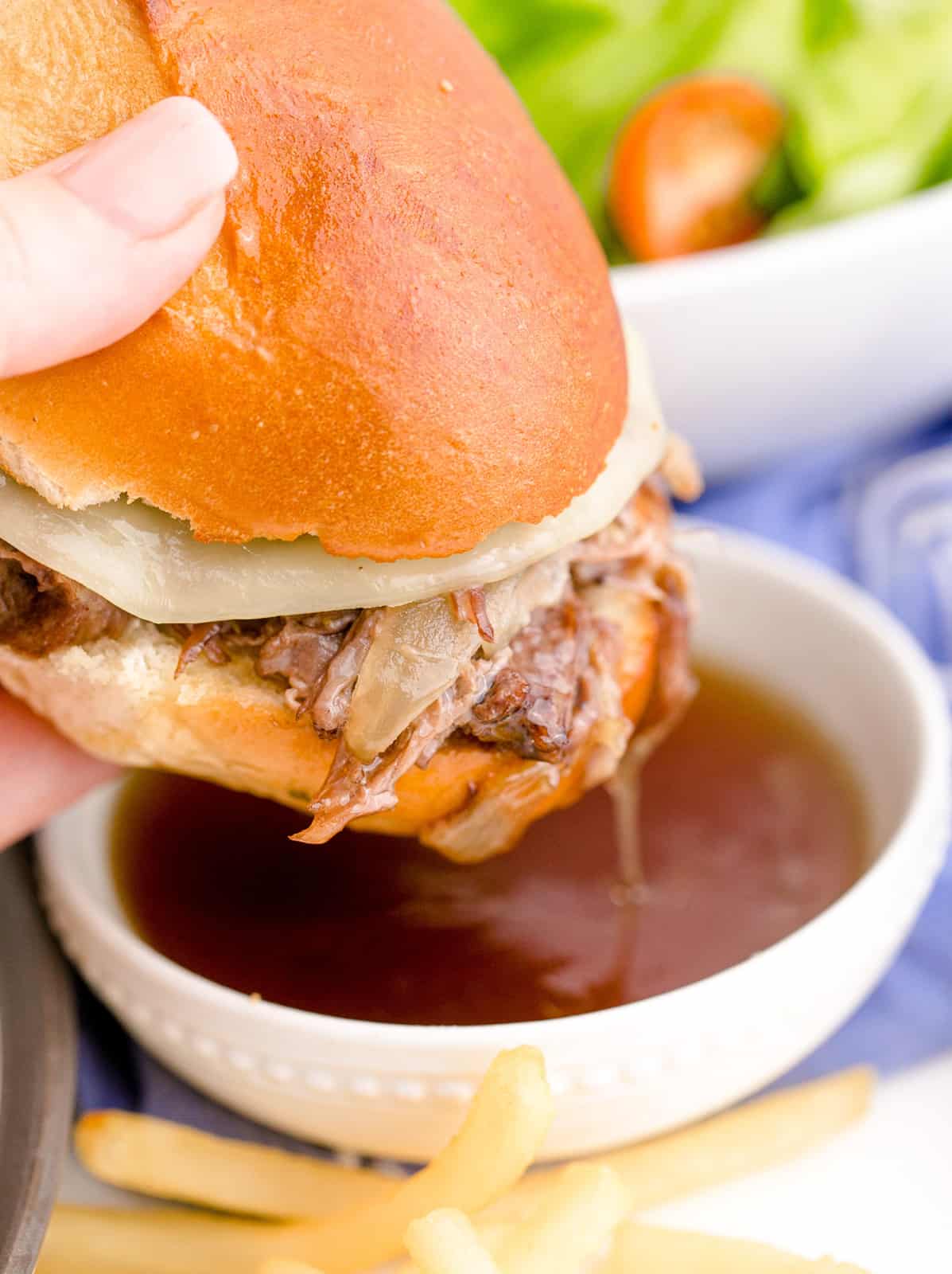 Hand dipping one Crockpot French Dips into au jus.