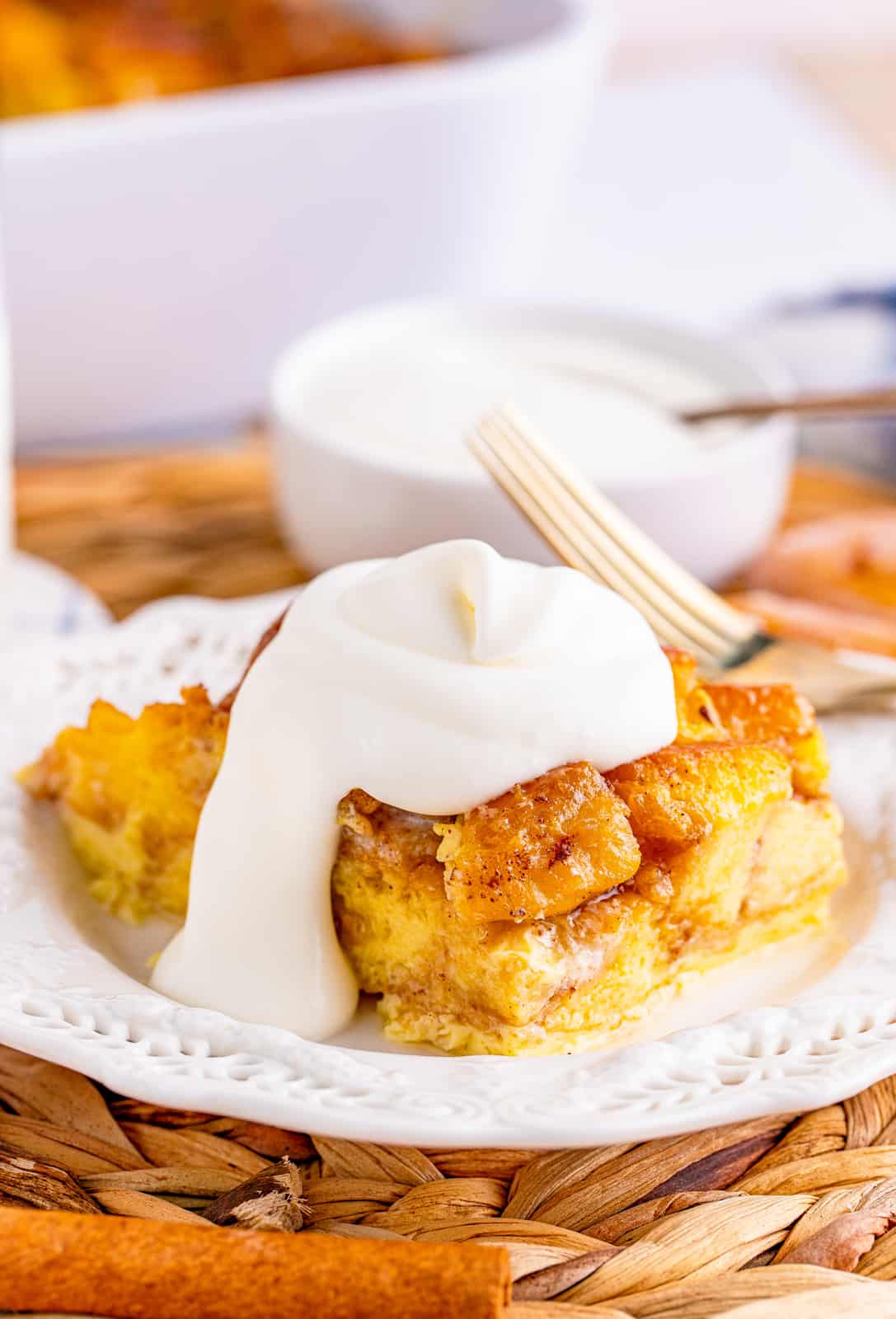 Slice of Honey Bun Bread Pudding on white plate topped with whipped topping.