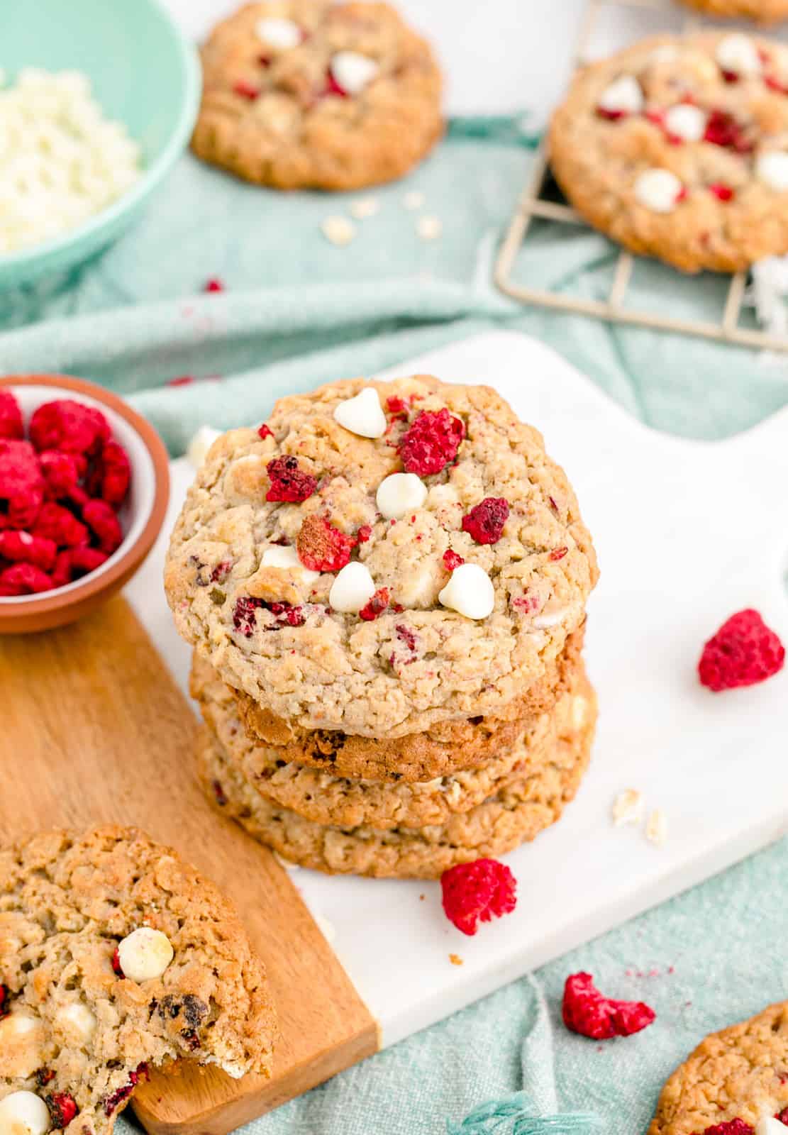 Stacked Oatmeal Raspberry White Chocolate Cookies with raspberries and other cookies around it.