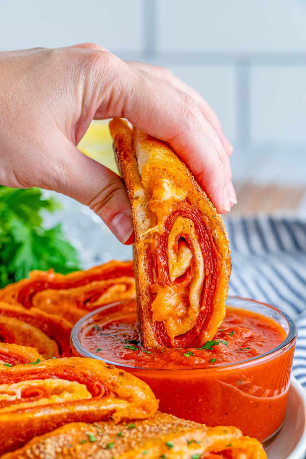 Hand dipping a slice of Pepperoni Stromboli in pizza sauce.