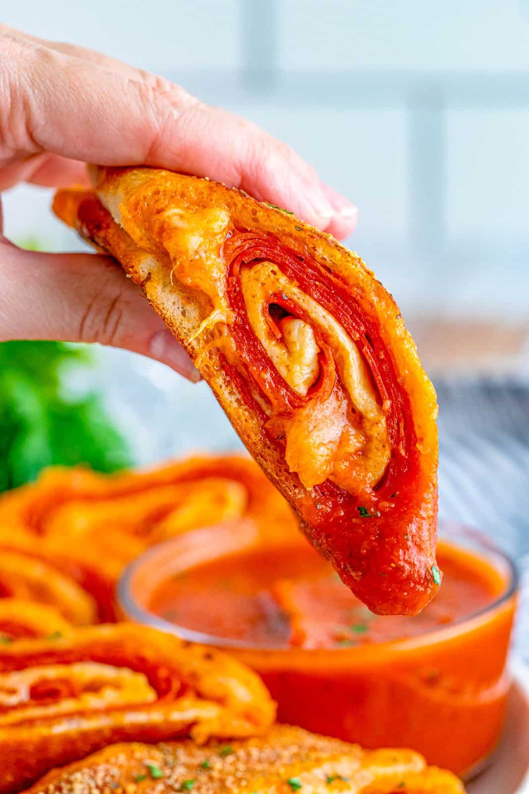 Hand holding up slice of Pepperoni Stromboli showing it dipped in pizza sauce.