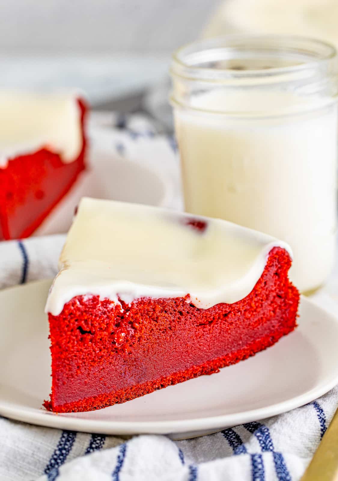 Slice of Red Velvet Ricotta Cake on white plate with milk in the background.
