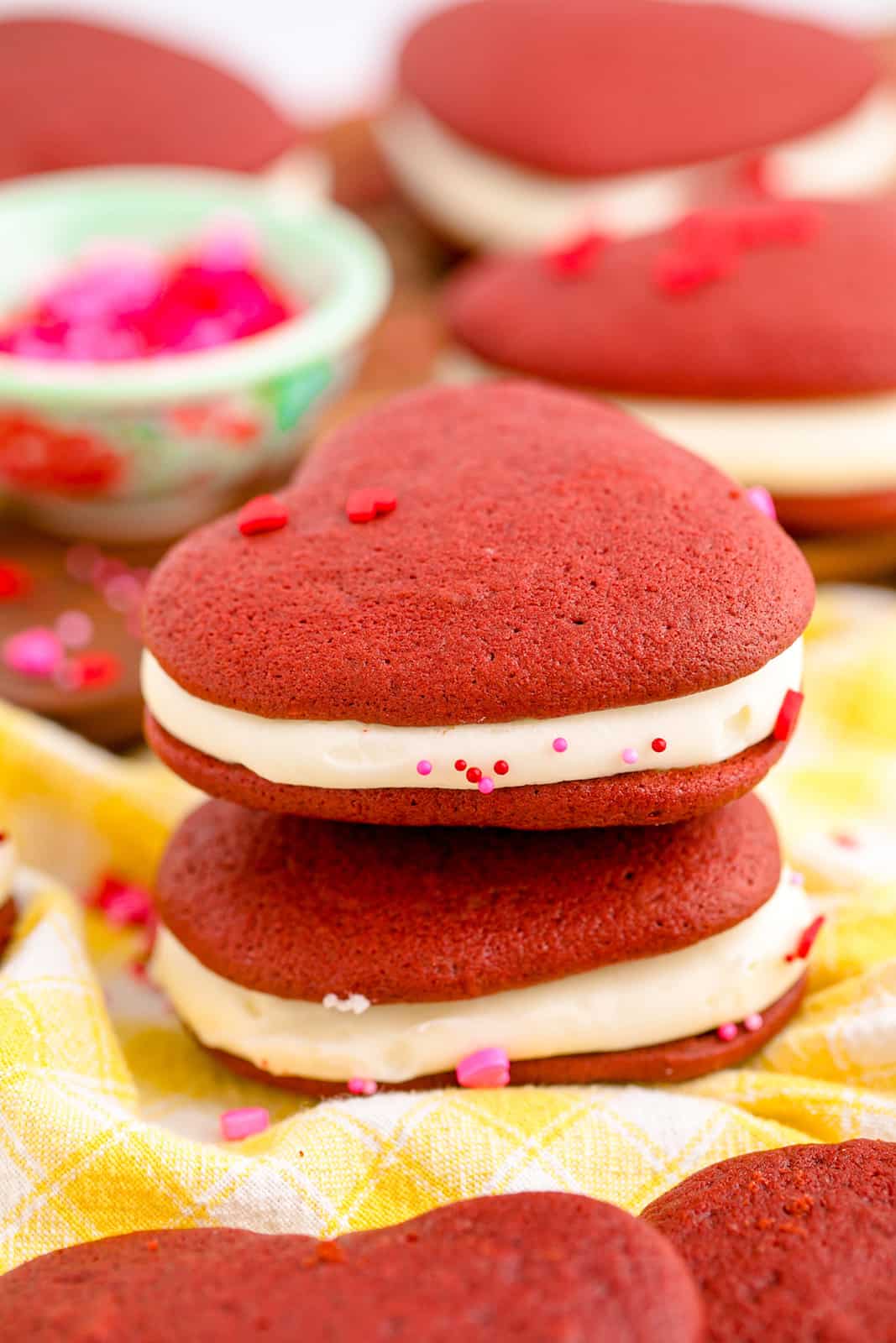 Two stacked Red Velvet Whoopie Pies on yellow linen with sprinkles.
