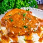 Square image of pork chops over mashed potatoes with gravy.