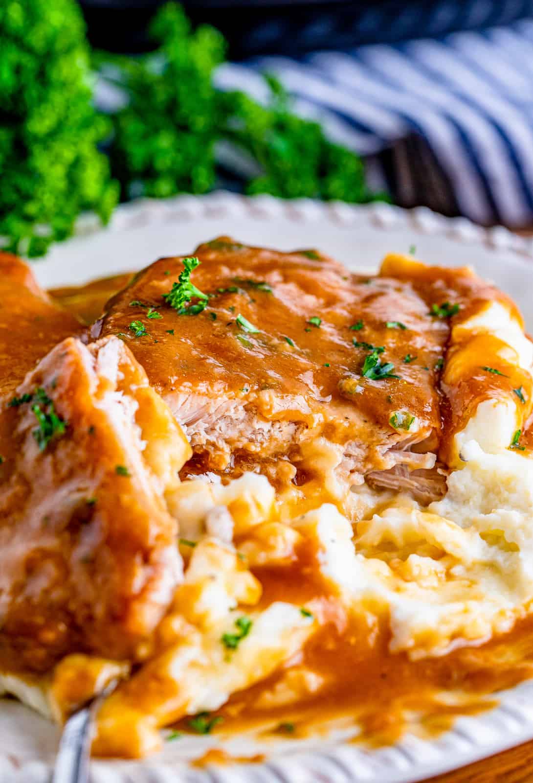 Cut Slow Cooker Pork Chops on plate with mashed potatoes and gravy.