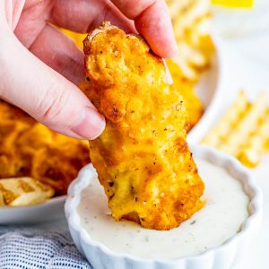 Square image of hand dipping one chicken tender in ranch.