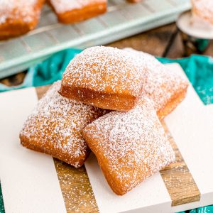 Square image of stacked Beignets on square board.
