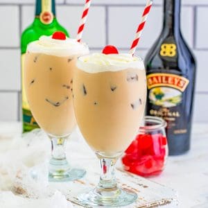 Square photo of two drinks topped with whipped cream and cherries.