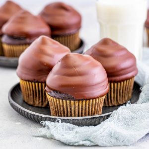 Square image of three cupcakes on metal plate with milk in background.