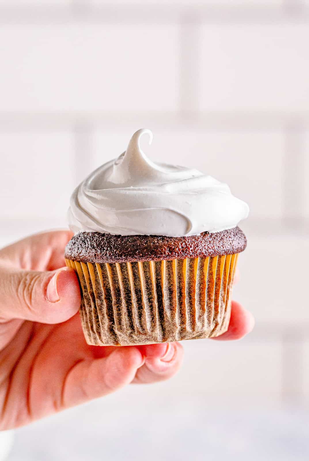 Hand holding up a cupcake with Marshmallow Frosting on it.