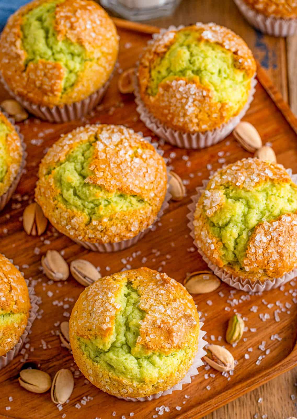 Overhead of Pistachio Muffins on a wooden board with pistachios around them.
