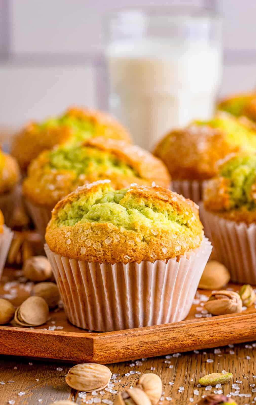 Pistachio Muffins on wooden board with muffins behind it with pistachios.