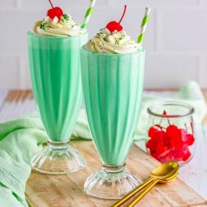 Square image of two Shamrock Shakes topped with whipped cream and cherries.